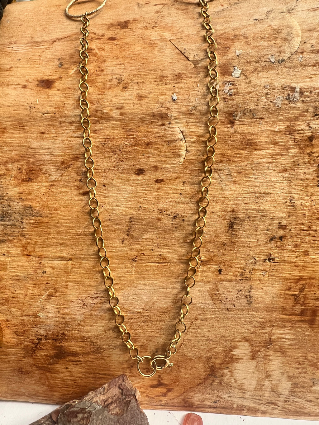 The gold-filled curb chain of the coin peridot necklace, displayed on a rustic wooden surface.