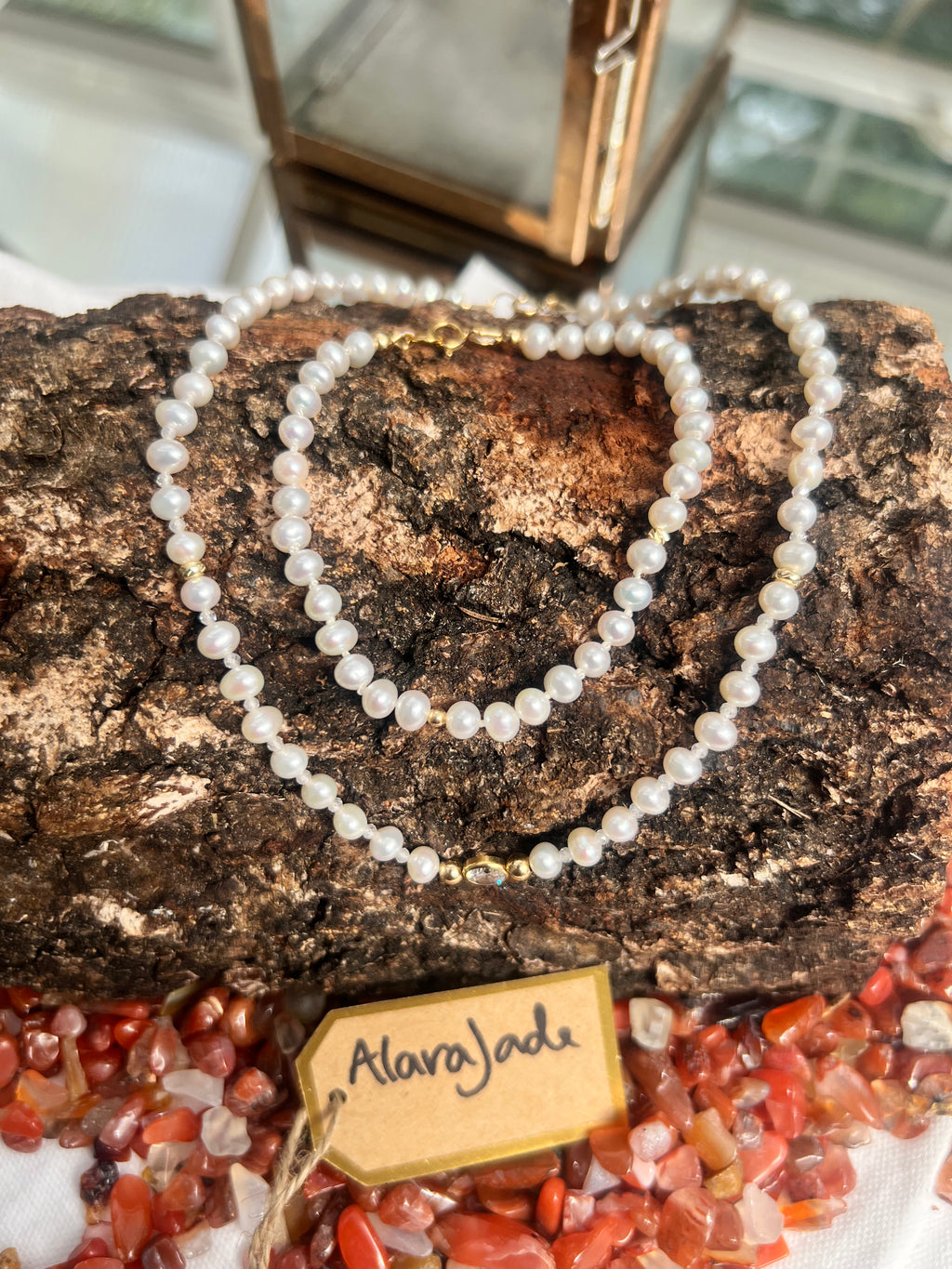 A pearl necklace and bracelet with gold-toned accents and clasp, draped over a textured piece of bark. 